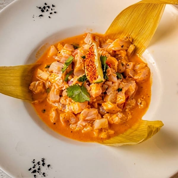 Peruvian ceviche with shrimp and fish in orange sauce, garnished with lime and corn husks.