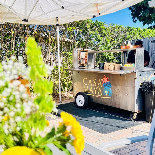 Casa Maya food cart with two staff members under a white tent on a sunny patio.