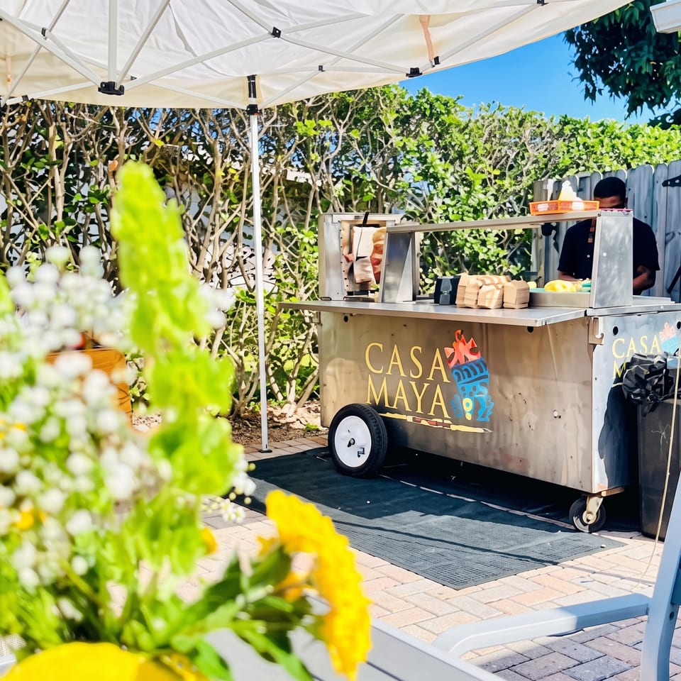 Casa Maya food cart with two staff members under a white tent on a sunny patio.