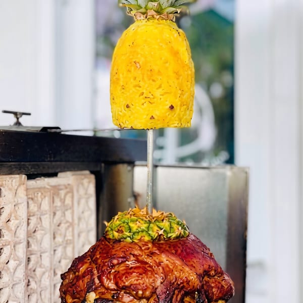 Al pastor meat cooking on a vertical rotisserie, topped with a pineapple.