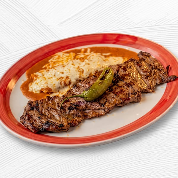 Grilled skirt steak with a green chili pepper, alongside cheesy enchiladas in red sauce on a white plate.