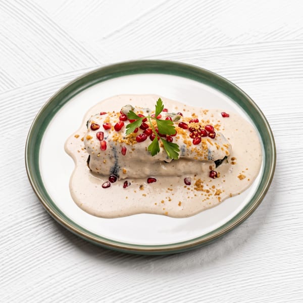 Chiles en nogada, a Mexican dish, on a white plate with green rim, garnished with pomegranate seeds and parsley.