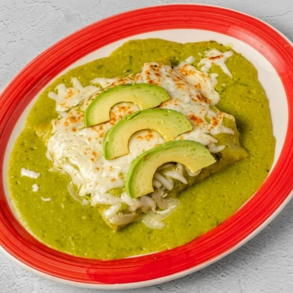 Green enchiladas topped with melted cheese and sliced avocado on a red-rimmed plate.