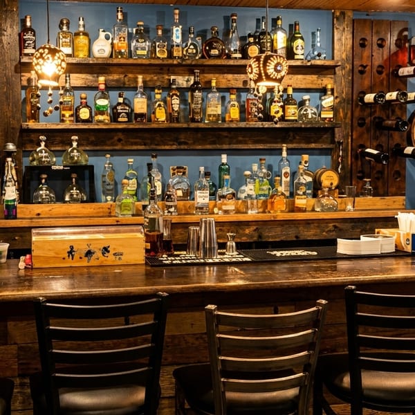 A rustic bar with a wooden counter, shelves of liquor bottles, and wine racks against a blue wall.
